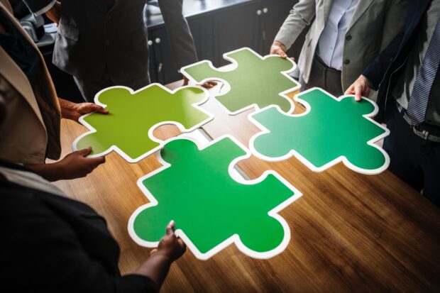 business people standing around a table holding giant plastic jigsaw pieces